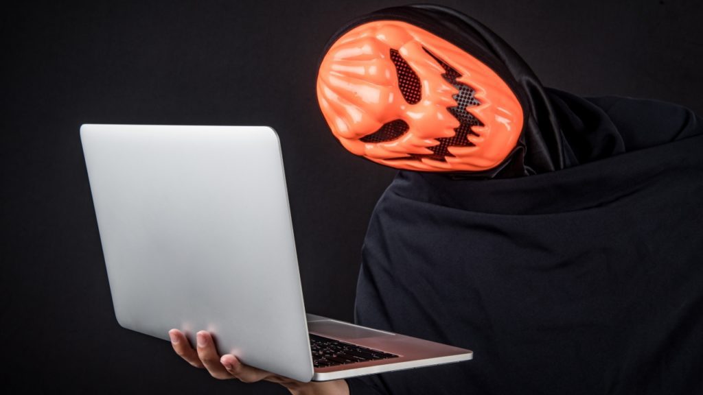 person wearing scary mask holding laptop