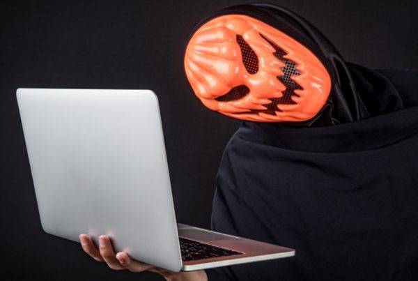 person wearing scary mask holding laptop